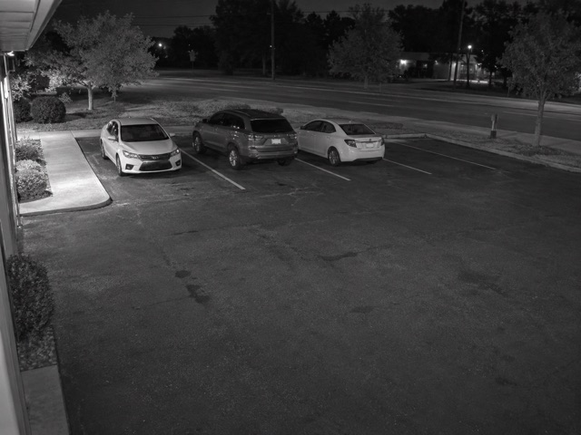 Conceptual infrared surveillance view of a business parking lot and the road beyond at night
