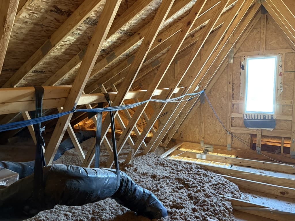 Blue and black low-voltage cables routed across wooden roof framing in an insulated residential attic.