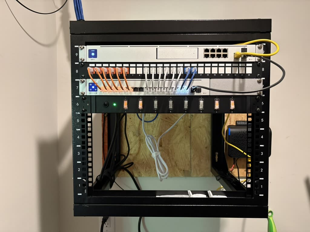 Wall-mounted equipment rack containing patch panels, network equipment, and organized colored patch cables.